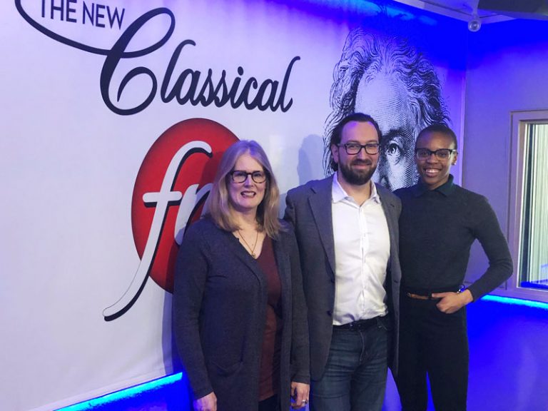 Image of Dr. Kathleen Gallagher, Amaka Umeh and Marc Wigmore in front of a white wall with the Classical FM logo, for the radio show The Oasis