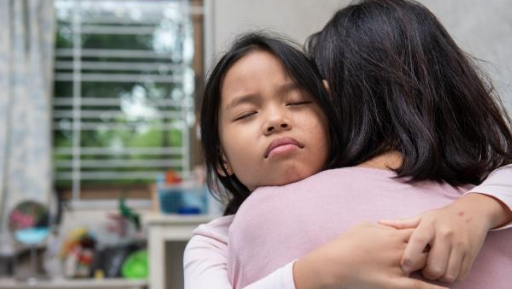 A child hugging a parent. The child's eyes are closed.