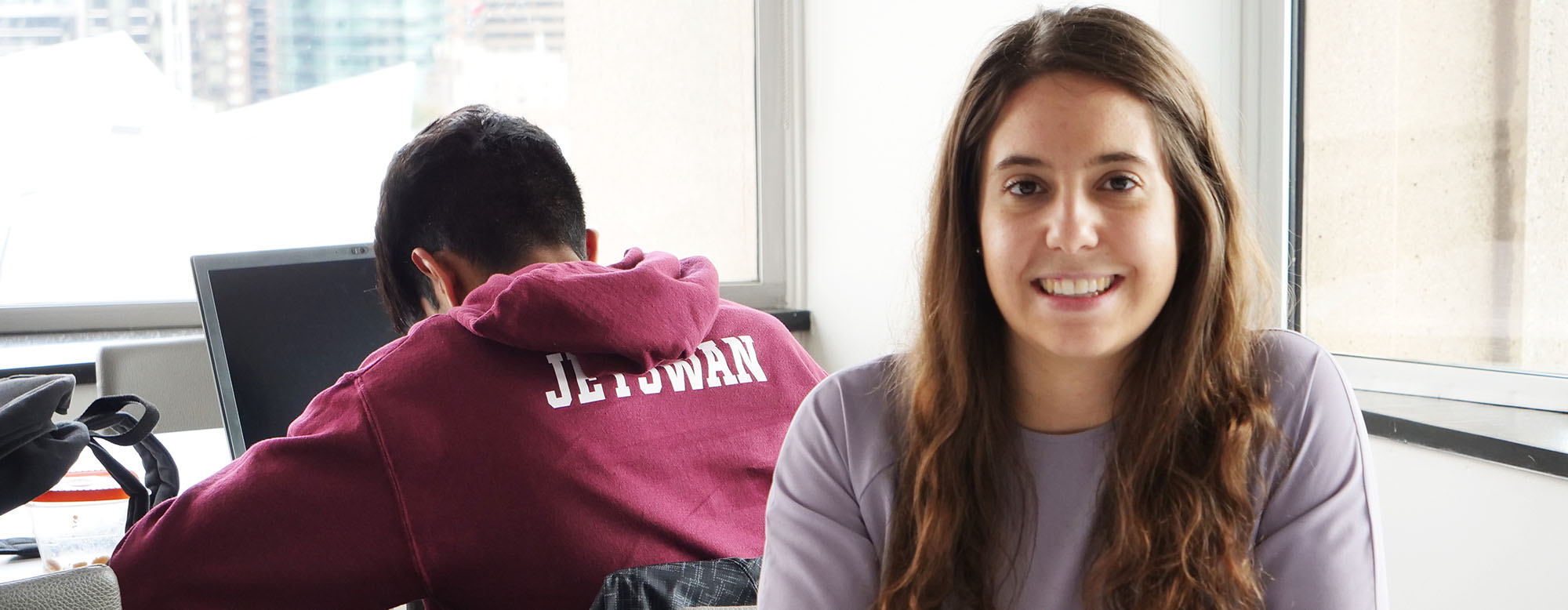 Two students in an OISE classroom. One is facing the camera, one has their back turned.