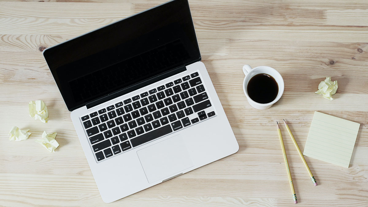 A laptop, coffee, and some writing tools on a desk.