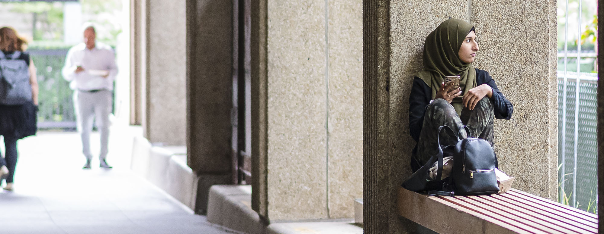 A student sitting outside the OISE building on a bench.