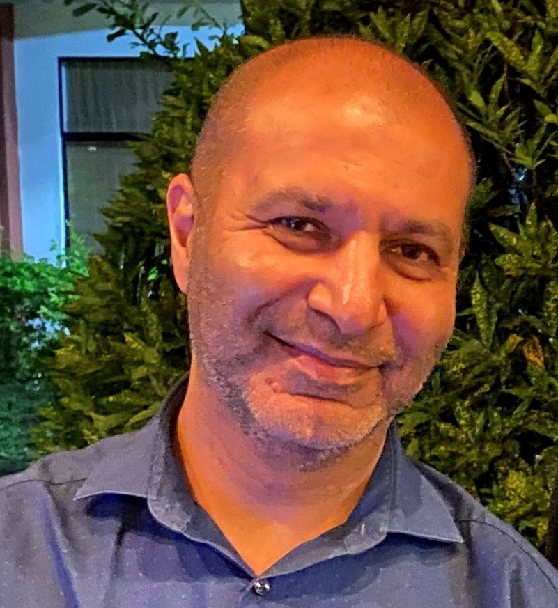 Image of a bald man, smiling, wearing a grey, collared shirt.