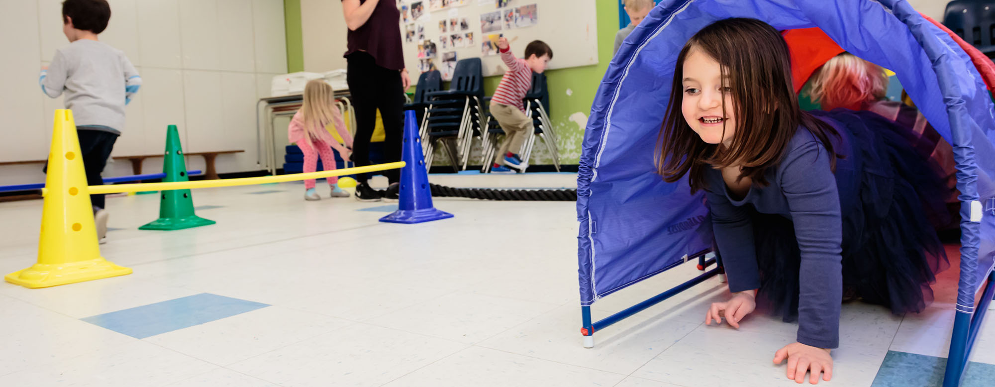 A JICS student crawling through a pop up toy tunnel.