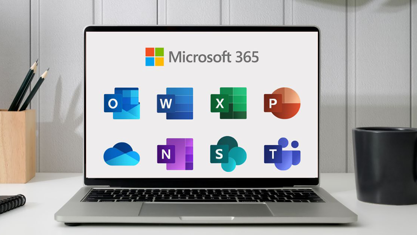 A silver laptop is sitting on white desk. On the screen, logos for different Microsoft 365 apps are visible in two rows: Outlook, Word, Excel, and Powerpoint in the top row, and OneDrive, Notes, Sharepoint, and Teams in the bottom row.