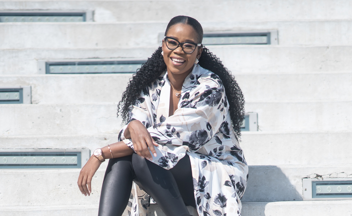 Stephanie Duff, a Black woman with long black hair and wearing glasses, is sitting and smiling at the camera