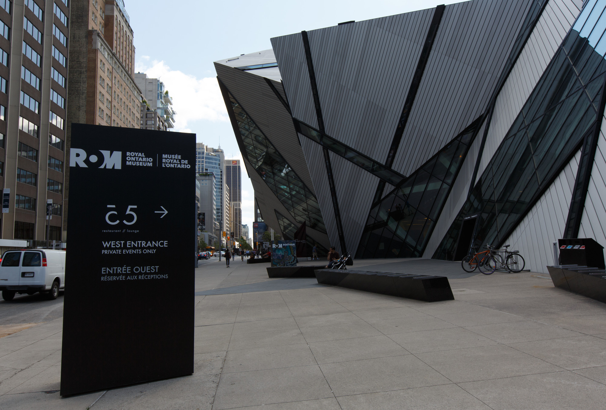 A brown sign post identifying a large angular glass and steel building as the Royal Ontario Museum