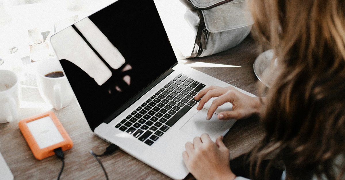 A person typing on a laptop, with a hard drive beside their device.