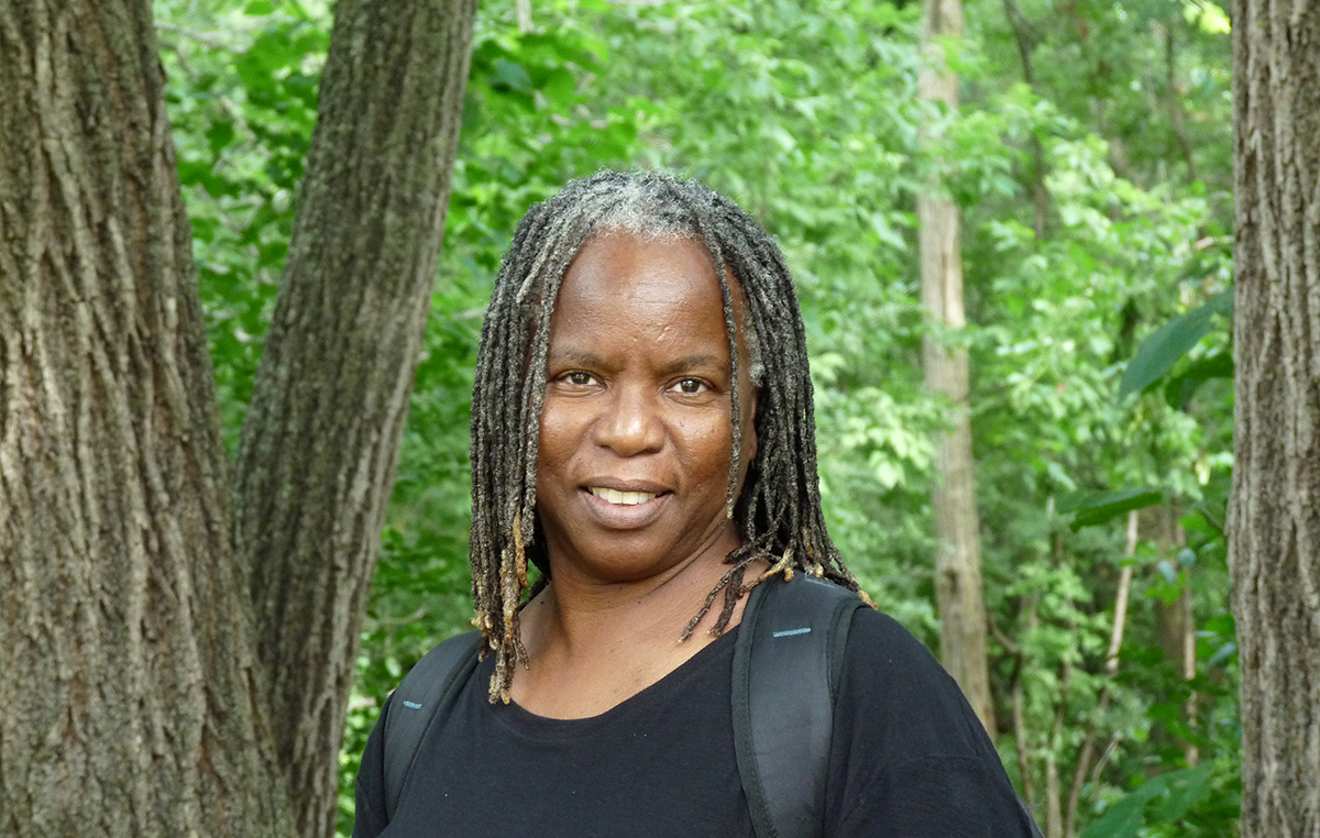 Woman with black top, standing in a forest, smiling