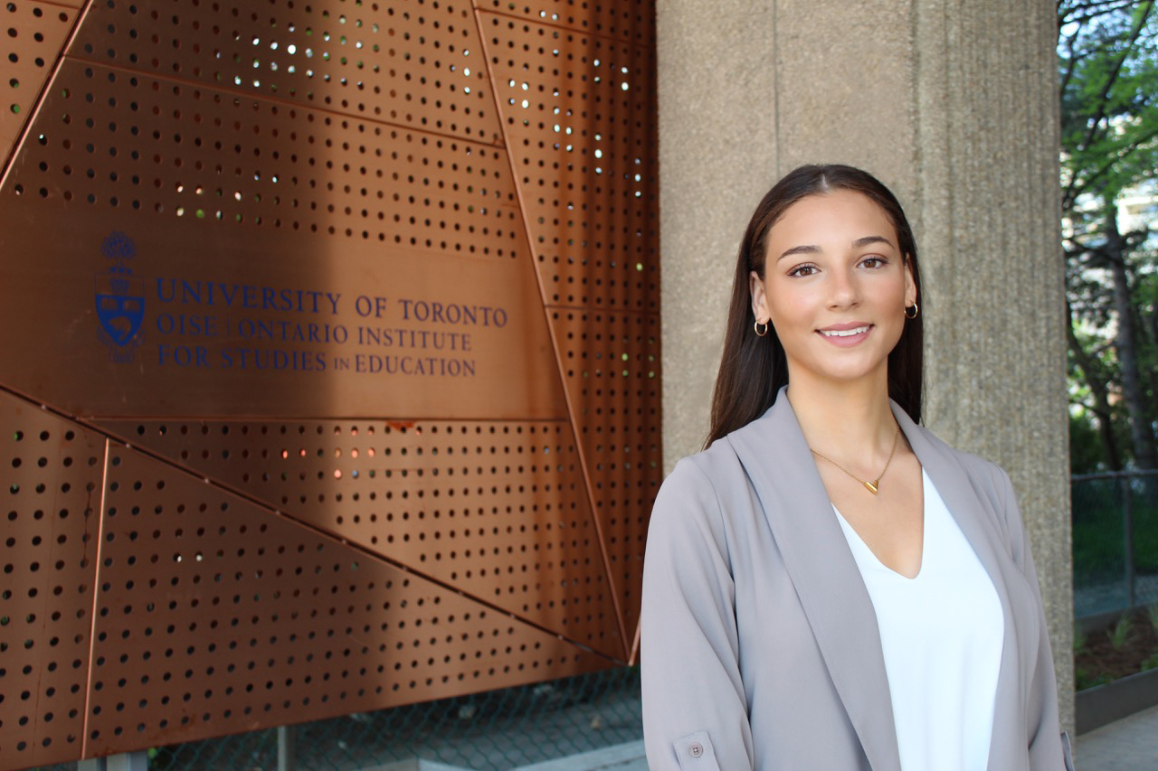 a woman standing in front of a sign that reads "University of Toronto, OISE Ontario Institute for Studies in Education.