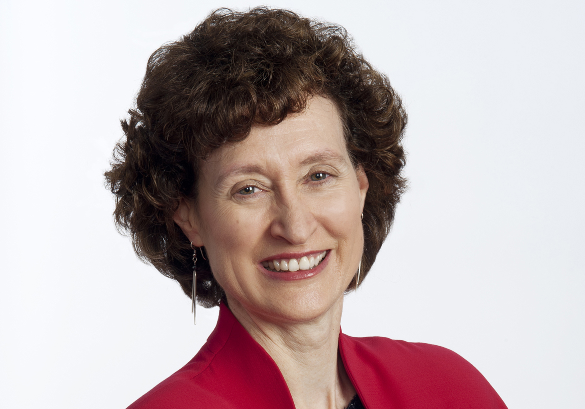 Smiling woman with short, curly hair wearing a red jacket, posed against a plain white background.