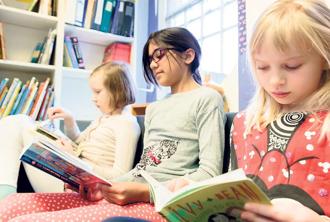 Three school children reading books in a library.