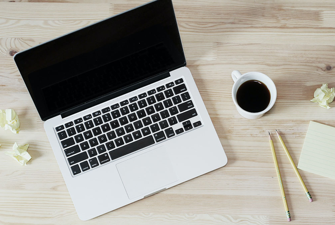 A laptop, coffee, and some writing tools on a desk.