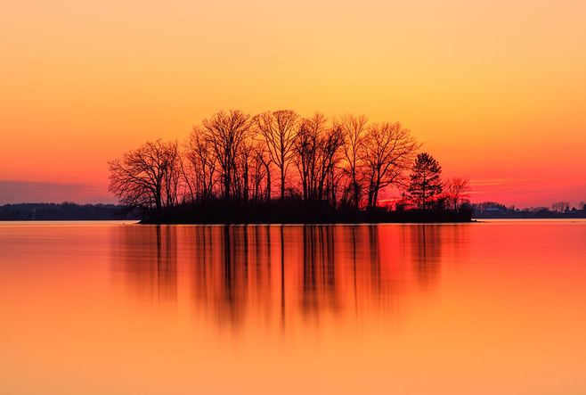 A sun setting with trees in the background and water in the foreground.