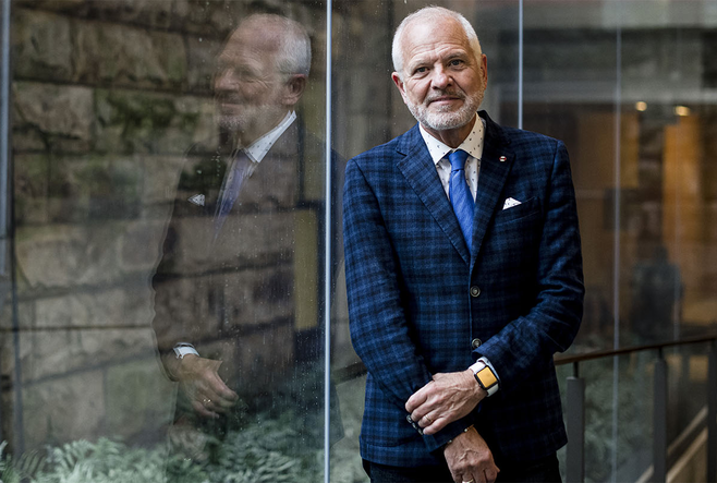 OISE Dean Normand in a blue suite smiling as he leans against a glass wall