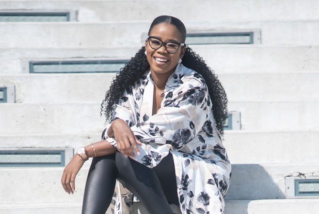 Stephanie Duff, a Black woman with long black hair and wearing glasses, is sitting and smiling at the camera