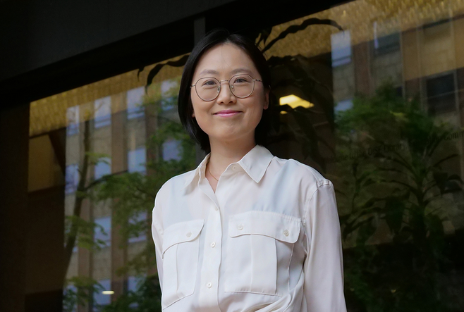 Lu Wang, a young Chinese woman, is wearing glasses and a white blouse, and smiling at the camera.