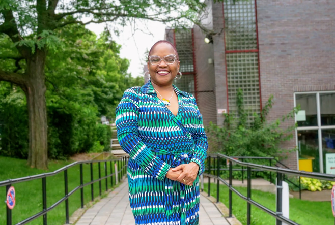 A Black woman is standing on an accessibility ramp with a big smile on her face 