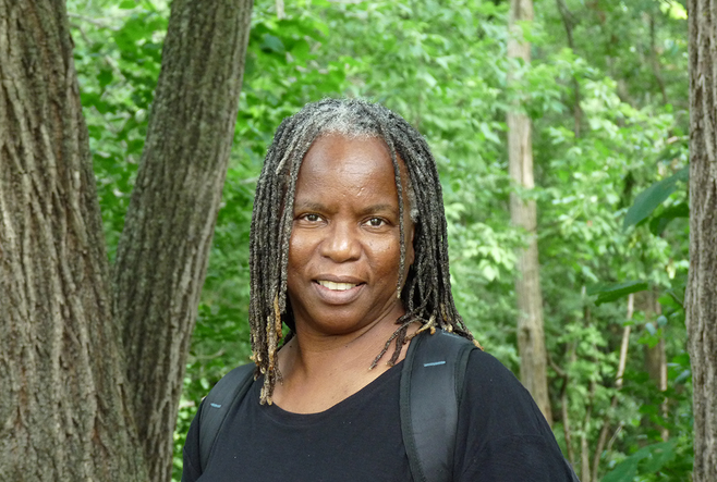 Woman with black top, standing in a forest, smiling