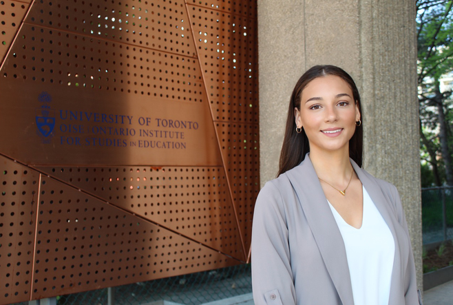 a woman standing in front of a sign that reads "University of Toronto, OISE Ontario Institute for Studies in Education.