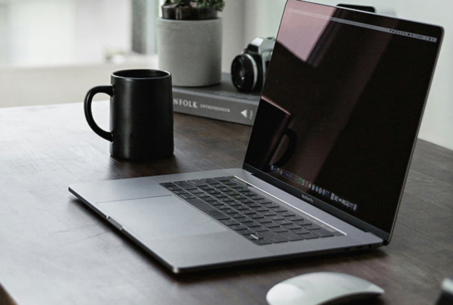 A laptop on a desk with a mug beside it.