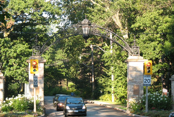 cars leaving through stone gate with trees in background