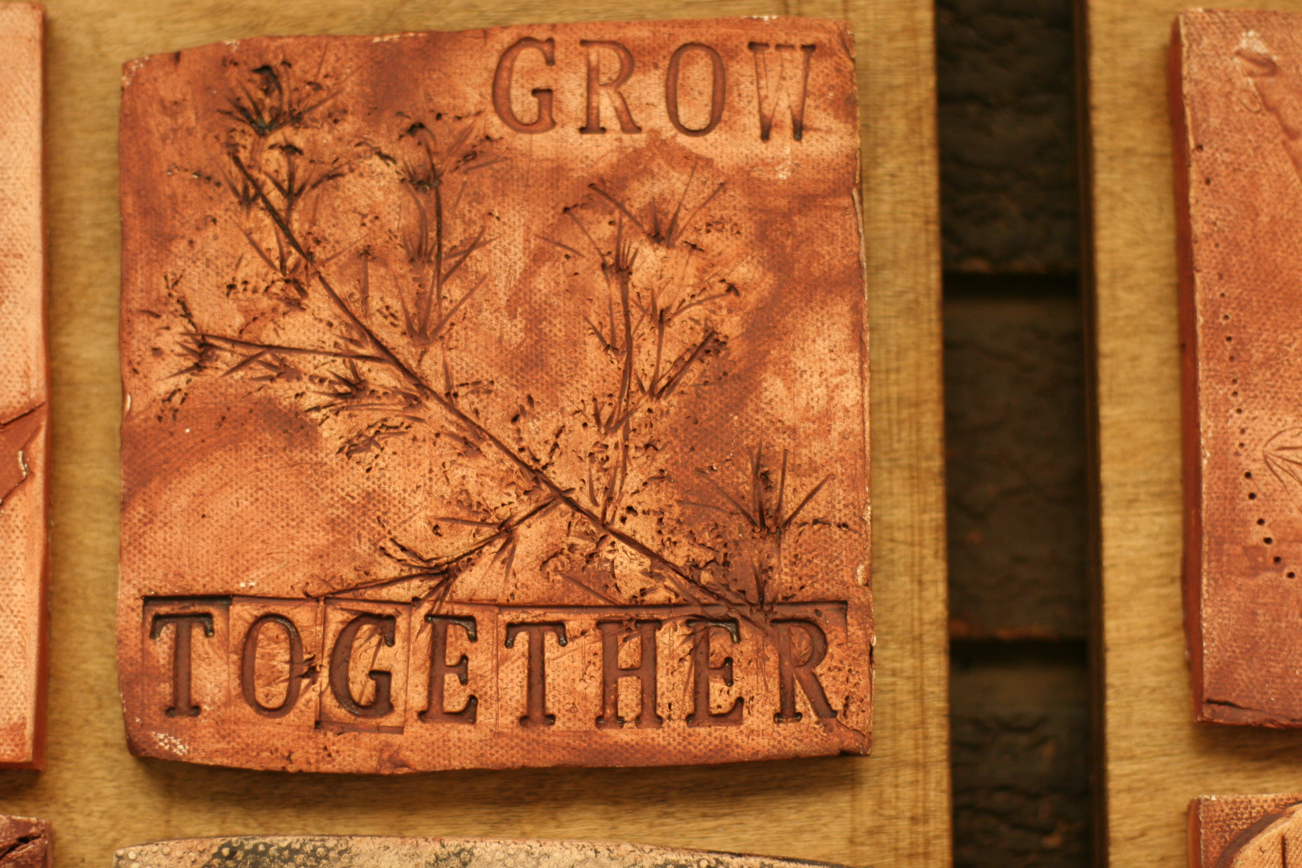 terracota ceramic tile with a leaf and the words 'grow together' engraved