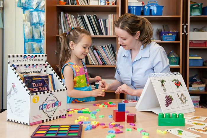 Student and teacher at a round table with toy blocks on it.