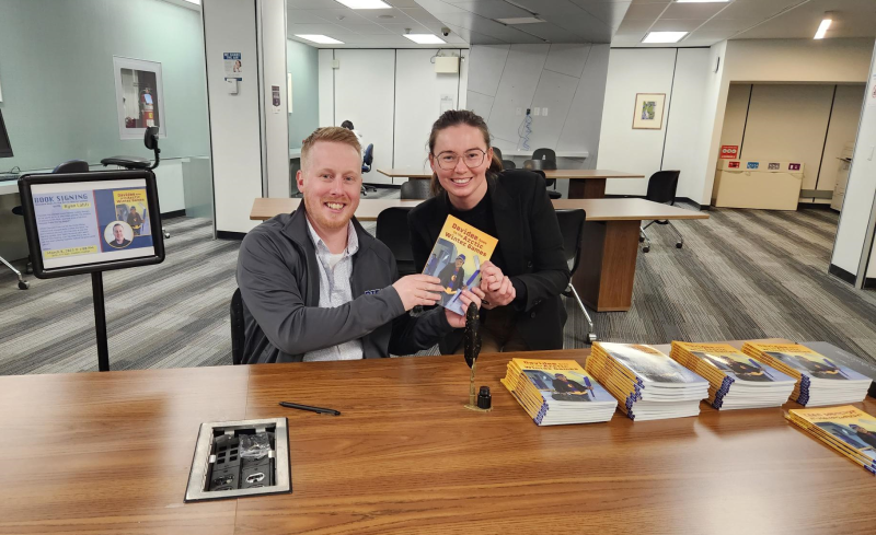 OISE Education Commons Technology Adoption Consultant Ryan Lahti holds up a copy of his book, Davidee Goes to the Arctic Winter Games, with OISE's Tessa Barclay from the Chief Administrative Office.