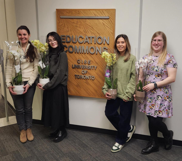 The women of Education Commons holding flowers and standing in front of the Education Commons sign on the third floor.