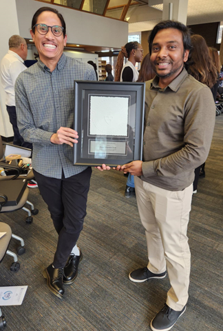 Education Commons' Drupal Developers, Jed Dela Cruz and Hentry Mathias, celebrate the award they won at the 2023 OISE Staff Excellence Awards. Jed is wearing a grey checkered shirt with dark blue pants while Hentry is wearing an olive shirt with chinos.