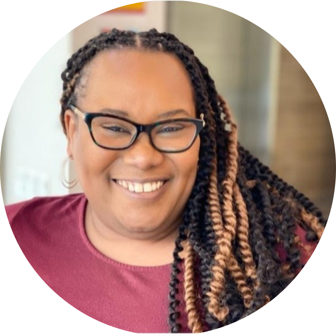 Devonnia Miller wearing a maroon shirt and glasses, smiling at the camera with a light hallway out of focus behind her