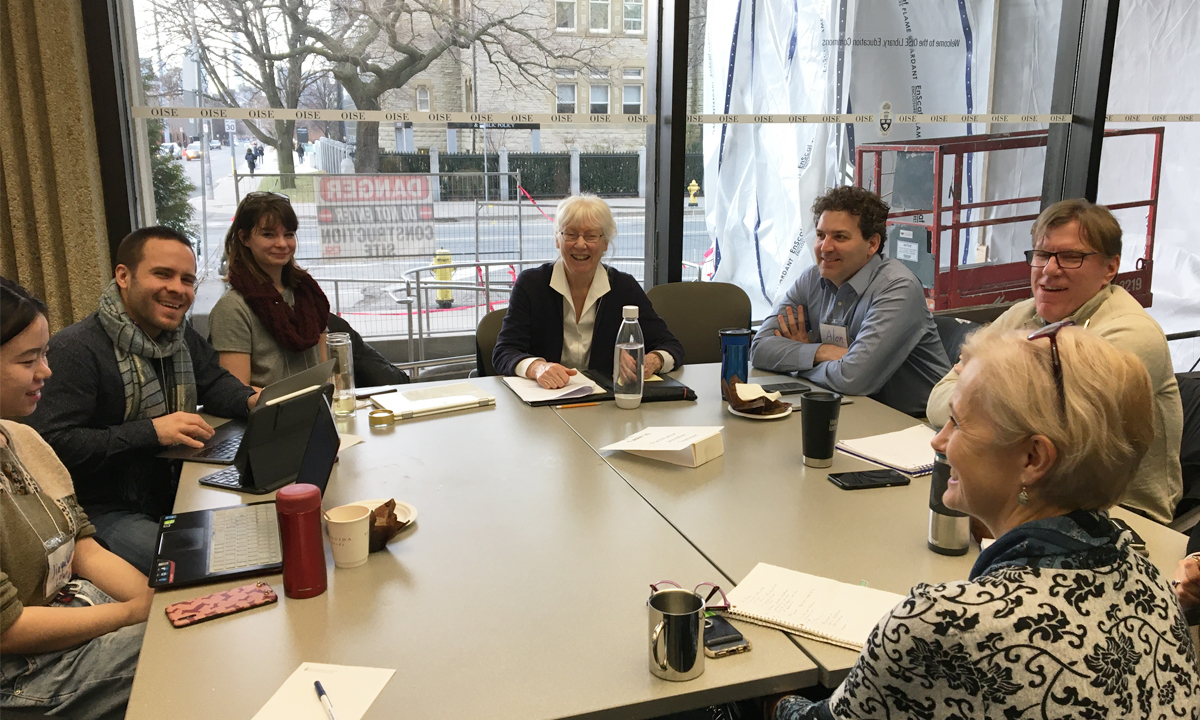 Group of men and women sitting around a table, smiling.