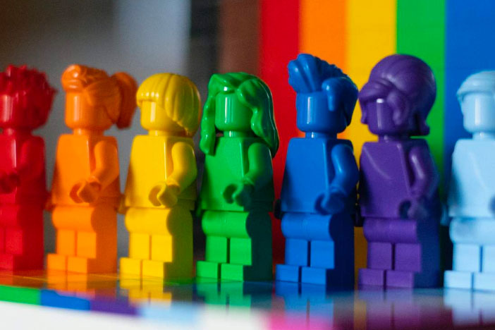 Rainbow colored Lego characters standing in front of a Pride flag background