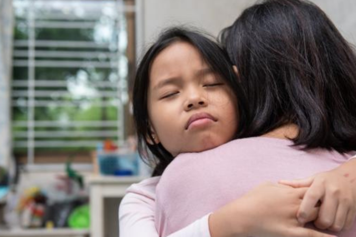 A child hugging a parent. The child's eyes are closed.