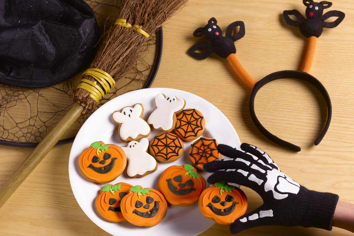 Person wearing skeleton glove picking up pumpkin cookie. 