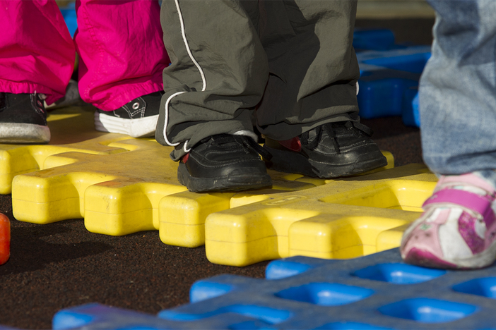 Four children playing on a playground puzzle. Only their shoes and the puzzle are visible.