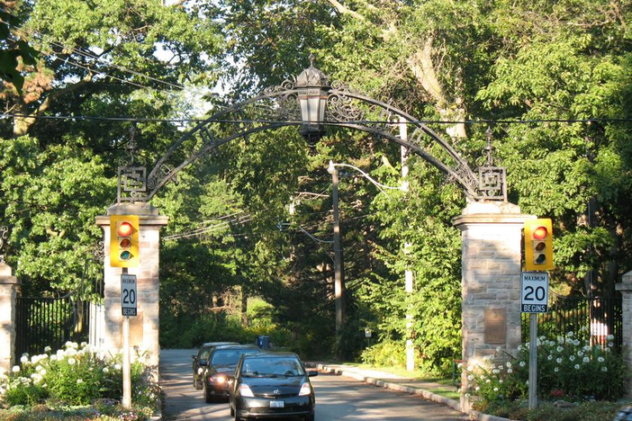 cars leaving through stone gate with trees in background