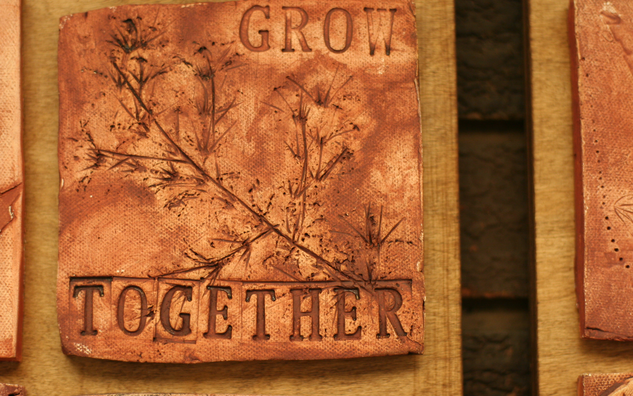 terracota ceramic tile with a leaf and the words 'grow together' engraved