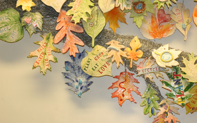 installation detail: orange, green, and blueish clay leaves on wire branch