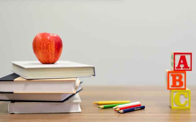 Books, pencils, an apple, and block letters on table.