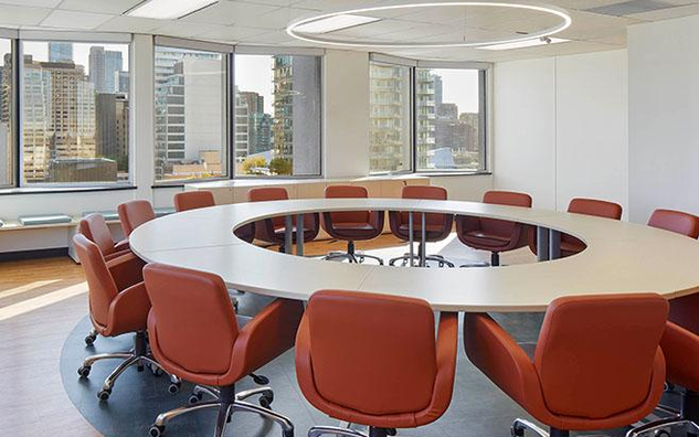 A meeting room with a round table with chairs surrounding it.