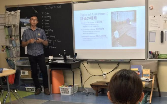 A teacher giving a presentation in front of a blackboard and projector screen. 