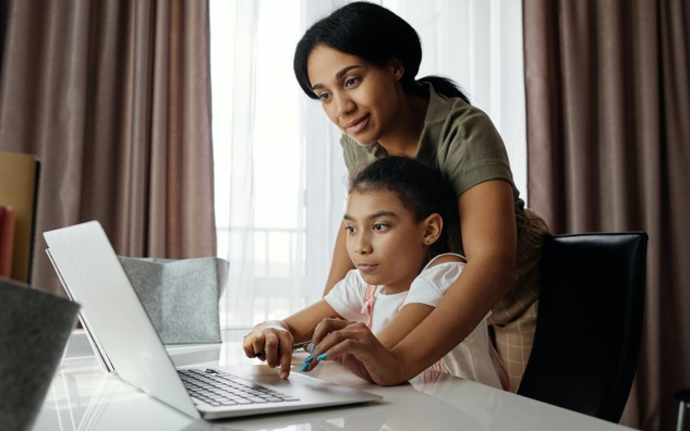 A mother is showing her daughter how to find something on their home laptop.