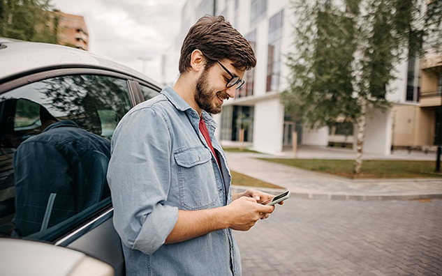 A person using a mobile phone and leaning on a car.