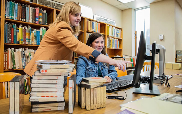 Two people using a desktop computer in a library.