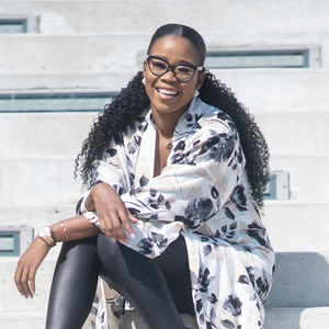 Stephanie Duff, a Black woman with long black hair and wearing glasses, is sitting and smiling at the camera