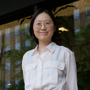 Lu Wang, a young Chinese woman, is wearing glasses and a white blouse, and smiling at the camera.