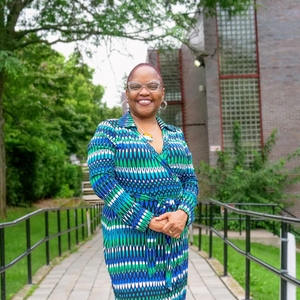 A Black woman is standing on an accessibility ramp with a big smile on her face 