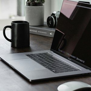 A laptop on a desk with a mug beside it.