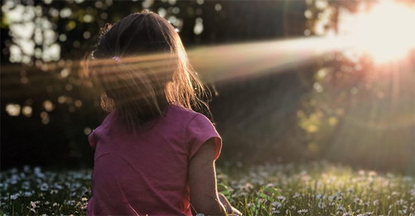 A ray of light hitting a child's face while they sit in a forest-like area.